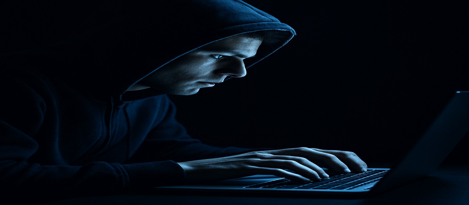 একজন ব্যক্তি অন্ধকারে ল্যাপটপে বসে একাগ্র দৃষ্টিতে good11 ওয়েবসাইটে অনলাইন গেমিং করছেন